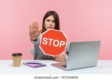 Frightened Assertive Woman Office Worker Showing Stop Gesture With Hand Holding Red Traffic Sign Of Prohibition, Blocking Harrassment At Workplace. Indoor Studio Shot Isolated On Pink Background