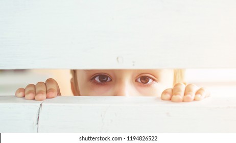 Frightened Child Is Spying Through A Wooden Fence. Scared Child Boy. Human Emotion, Facial Expression. Sad Kid Outdoors. Bored Little Boy