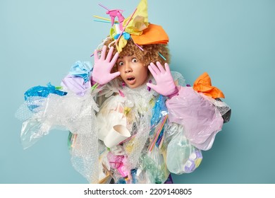 Frightened curly haired woman keeps palms towards camera in protective gesture afraids of something makes costume from wastes collects plastic garbage feels scared isolated over blue background - Shutterstock ID 2209140805