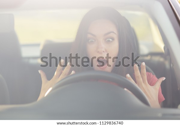 Frightened female going to drive car for first time\
by herself, keeps jaw dropped, stares at wheel, doesn`t know how\
start engine, has terrible facial expression, expresses\
surprisement and\
shock