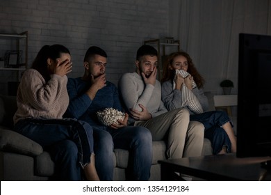 Frightened friends watching film and eating popcorn at home