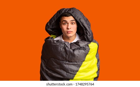 Frightened Guy Covered In Sleeping Bag Over Orange Studio Background