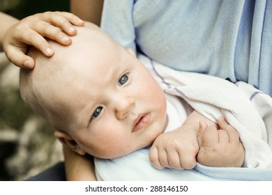 Frightened little baby boy resting in mothers arms in a sling wrap, his sibling caressing him on the head and comforting him. Family values, siblings love and affection concepts. 