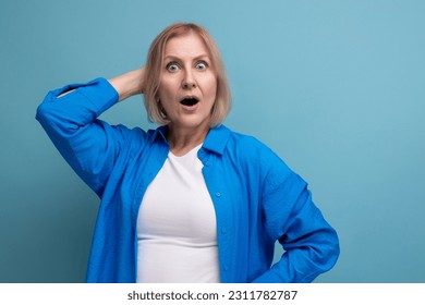 frightened middle-aged woman in a beautiful shirt on a blue background - Shutterstock ID 2311782787