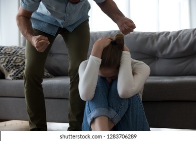 Frightened scared young defenseless woman victim hiding from aggressive man suffer from physical abuse, abusive husband threaten beat upset crying wife with fists, fear of domestic violence concept