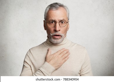 Frightened Shocked Bearded Man Has Beard Stares At Camera With Bated Breath, Hears Shocking News, Can`t Believe In Them, Isolated Over White Concrete Background. People, Pension, Reaction Concept