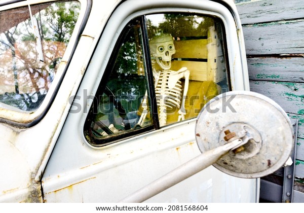 Frightened skeleton driver driving an old car\
looking in the rearview\
mirror