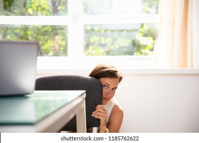 Frightened Young Businesswoman Hiding Behind Chair At Workplace