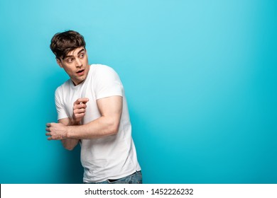 Frightened Young Man In White T-shirt Looking Back On Blue Background