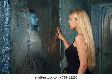 Frightened young woman looking in the mirror and seeing in reflection a ghost girl