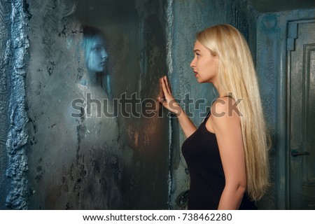 Frightened young woman looking in the mirror and seeing in reflection a ghost girl