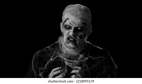 Frightening Man With Halloween Zombie Bloody Wounded Face Make-up, Scared By Police Lights. Horror Theme. Sinister Undead Guy Isolated On Studio Black Background. Voodoo Rituals. Detention Of Criminal