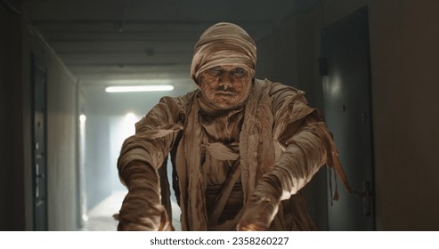 Frightening undead Egyptian mummy in bandages moving in corridor of old cursed house. Guy in halloween costume pretending to be a zombie - halloween concept 