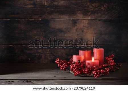 Frist Advent with red berry decoration and candles in a wreath, one is lighted, holiday home decor against a dark rustic wooden background, copy space, selected focus, narrow depth of field