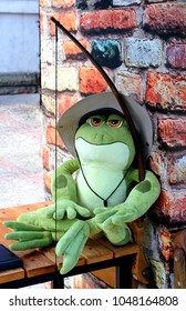 A frog in hat and businesslike appearance sits and bow at the brick wall   waits for the prince  Green plush toy frog 