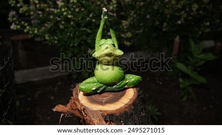 A frog statue is sitting on a log in a garden. The frog is in a pose that looks like it is meditating