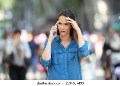 Fronf view of a worried woman talks on the phone walking in the street - Powered by Shutterstock