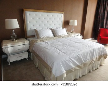 Front Angle Of A King Size Bed In An Upscale Hotel Room, With Marble Topped Night Stands And Lamp Shades