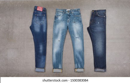 Front and back view three light, blue, torn jeans close-up. –gray background

