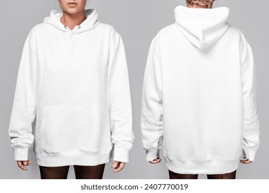 Front and back views of a woman wearing a white, oversized hoodie with blank space, ideal for a mockup, set against gray background.