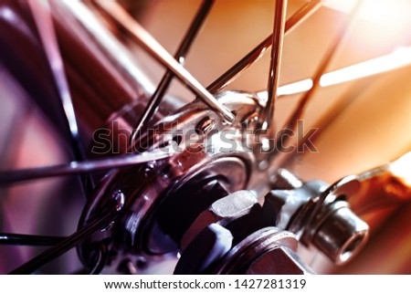 Front Bicycle wheel with spokes. The wheel sleeve is shiny metal. Spokes are chrome. The background is blurred.
