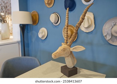 In front of a blue wall with several different straw hats stands a wooden head of a ibex as decoration - Powered by Shutterstock