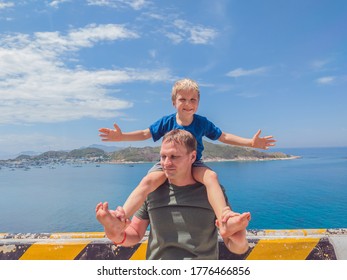 Front Boy Son Laugh Sitting On Fathers Shoulders. No Photoshop Sun On Skin. Sea, Clouds, Island Background. Funny Photo, Happiness Lifestyle, Father's Day, Love Parenthood, Family Holiday Concept