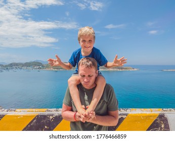 Front Boy Son Laugh Sitting On Fathers Shoulders. No Photoshop Sun On Skin. Sea, Clouds, Island Background. Funny Photo, Happiness Lifestyle, Father's Day, Love Parenthood, Family Holiday Concept