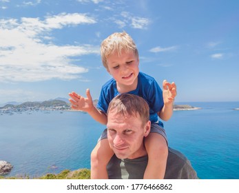 Front Boy Son Laugh Sitting On Fathers Shoulders. No Photoshop Sun On Skin. Sea, Clouds, Island Background. Funny Photo, Happiness Lifestyle, Father's Day, Love Parenthood, Family Holiday Concept