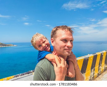 Front Boy Son Laugh Sitting On Fathers Shoulders. No Photoshop Sun On Skin. Sea, Clouds, Island Background. Funny Photo, Happiness Lifestyle, Father's Day, Love Parenthood, Family Holiday Concept