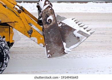 Front Bucket Of Excavator On Blurred Background Of Snowy Road. Side View