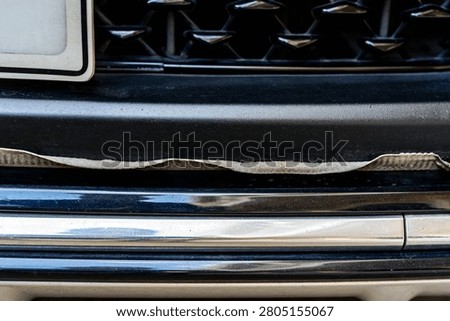 Front bumper show torn, detached, peeling and broken lower rubber skirt lip or trim beneath under grille. Vehicle wear and tear,  Damaged front bumper and torn rubber lip of car. Loss of adhesion.