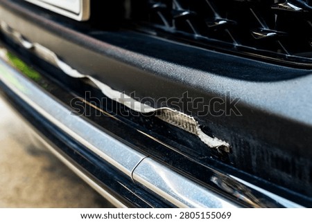 Front bumper show torn, detached, peeling and broken lower rubber skirt lip or trim beneath under grille. Vehicle wear and tear,  Damaged front bumper and torn rubber lip of car. Loss of adhesion.