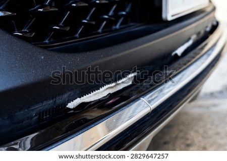 Front bumper show torn, detached, peeling and broken lower rubber skirt lip or trim beneath under grille. Vehicle wear and tear,  Damaged front bumper and torn rubber lip of car. Loss of adhesion.
