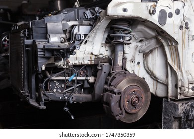 The Front Of The Car After An Accident With A Disassembled Body And Metal Elements And Assemblies Under The Hood In A Car Repair Shop Or Garage Against A Dark Background.