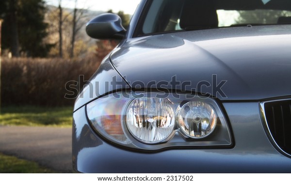 Front of a car with a blurred\
background. Metallic paint texture on car, not noise. Focus on\
lights.