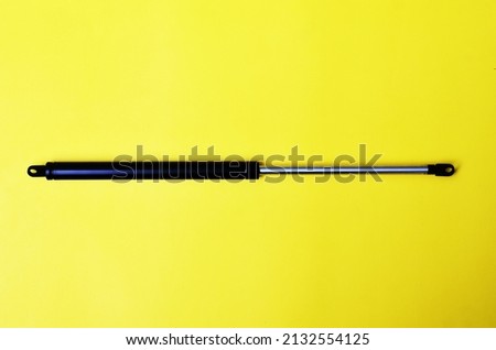 Front car engine hood shock absorber gas spring isolated on yellow background.