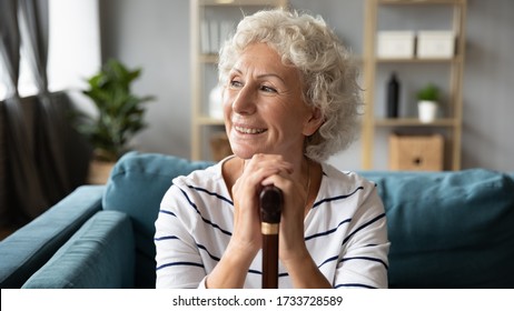 Front close up view dreamy positive middle aged senior woman relaxing on couch with walking cane in hands, thinking of future or recollecting good memories. Happy disabled grandmother resting at home. - Powered by Shutterstock