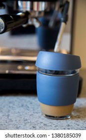 Front close up view of glass takeaway coffee cup with silicone sleeve and lid with espresso machine in the background on the kitchen bench - eco and budget friendly option to on the go hot beverages.