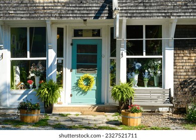 The front of a country style floral shop. The glass windows have multiple vases of colorful flowers. The wooden vintage green door has half glass and a yellow wreath hanging on the bottom of the door.