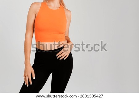 Front crop view of a model presenting a seamless bright orange workout crop top paired with high-waisted compression black leggings.