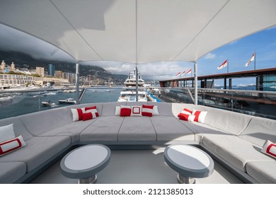 The front deck of huge yacht in port of Monaco at sunny day, landmarks of Monte-Carlo and a lot of motorboats are on background, the lounge zone for a chilling, megayacht is moored in marina