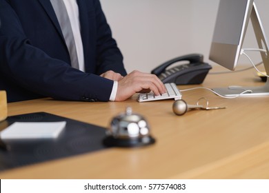 Front Desk Manager In A Hotel Typing Information On The Computer, Close Up Of His Hand , A Service Bell And Door Key