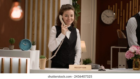 Front desk staff makes room reservations at hotel reception, using landline phone call to talk to guests about accommodation and bookings. Woman receptionist answering telephone. Handheld shot. - Powered by Shutterstock