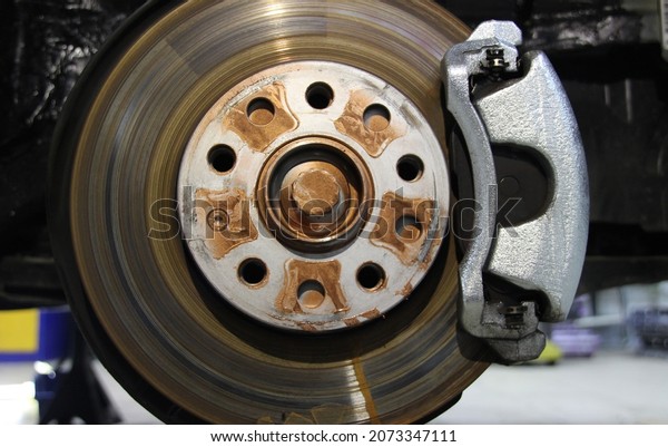 The front disc brake is a close-up on a car in the\
process of replacing a new tire. The rim is removed, showing the\
front rotor and caliper. Brake disc with hub before installing the\
tire.