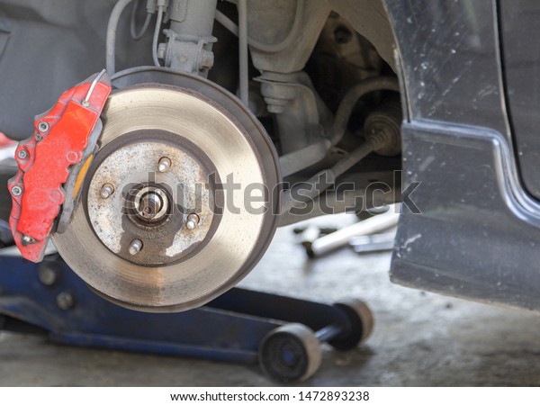Front disc brake on black color\
car with red cover brake caliper process of new tire\
replacement