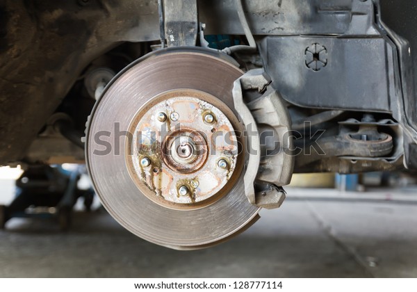 Front\
disk brake on car in process of damaged tyre replacement. The rim\
is removed showing the front rotor and\
caliper.