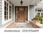 A front door and covered porch detail on a home with grey siding, white trim, red brick, a wooden front door.