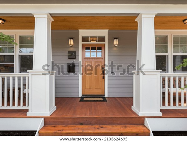Front door and covered porch of new home\
exterior: solid wood door is flanked by sconce lights and has glass\
panels in upper portion and\
mullions.