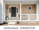 A front door detail with a stone accent wall, a black door, covered porch, white posts and railing, and grey siding.